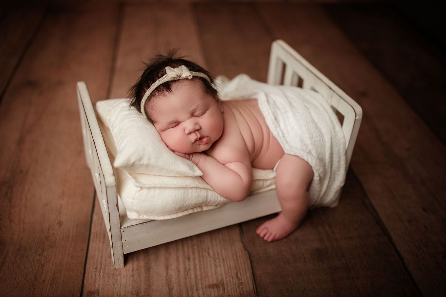 Peaceful newborn resting in white wooden bed on wooden floor.