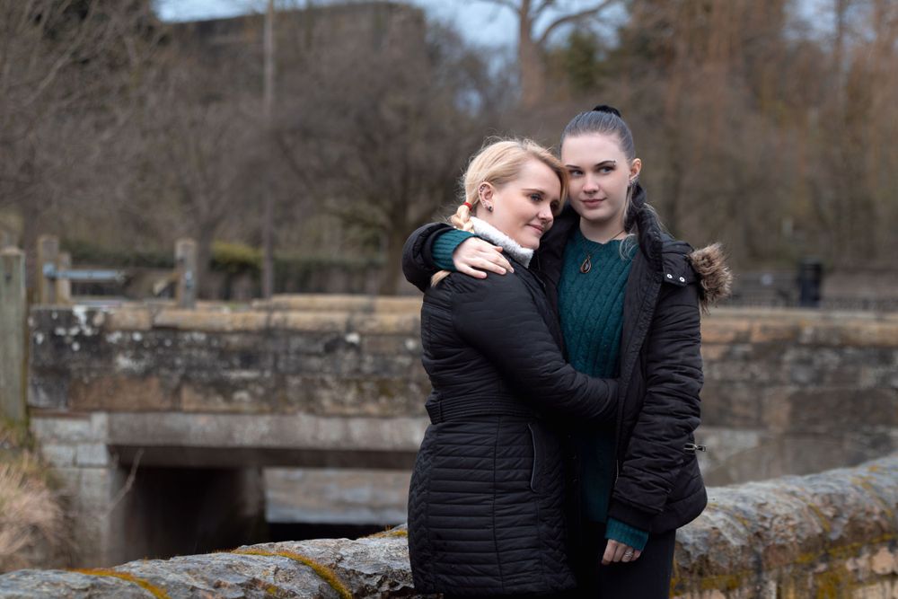 A couple embraces on a stone bridge during a winter day.