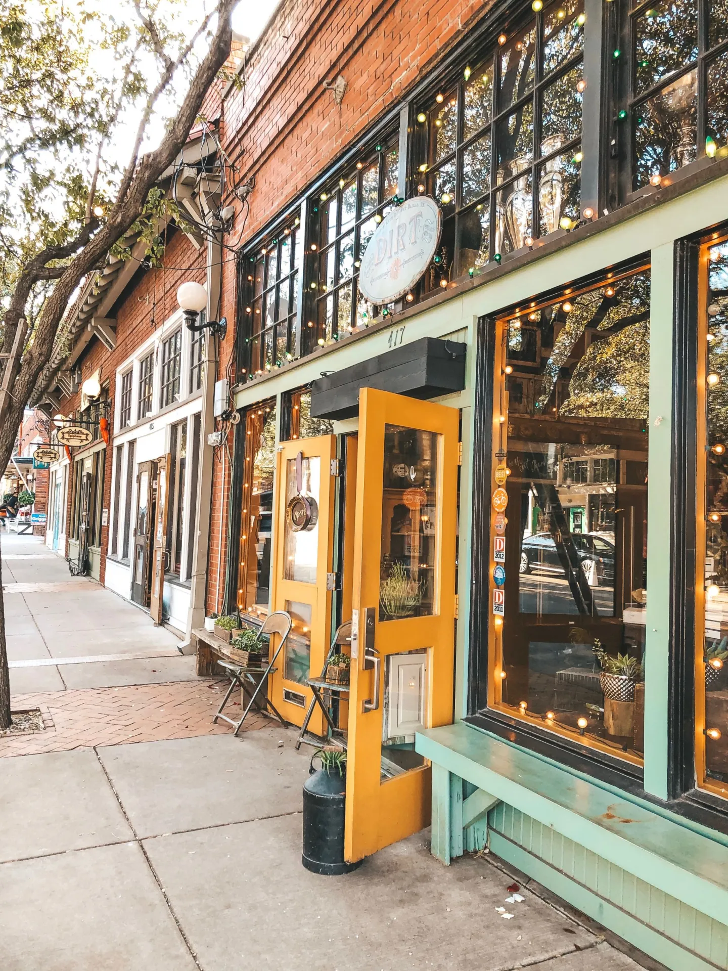 Row of storefronts with yellow doors and mint green trim along a sidewalk in an urban setting.