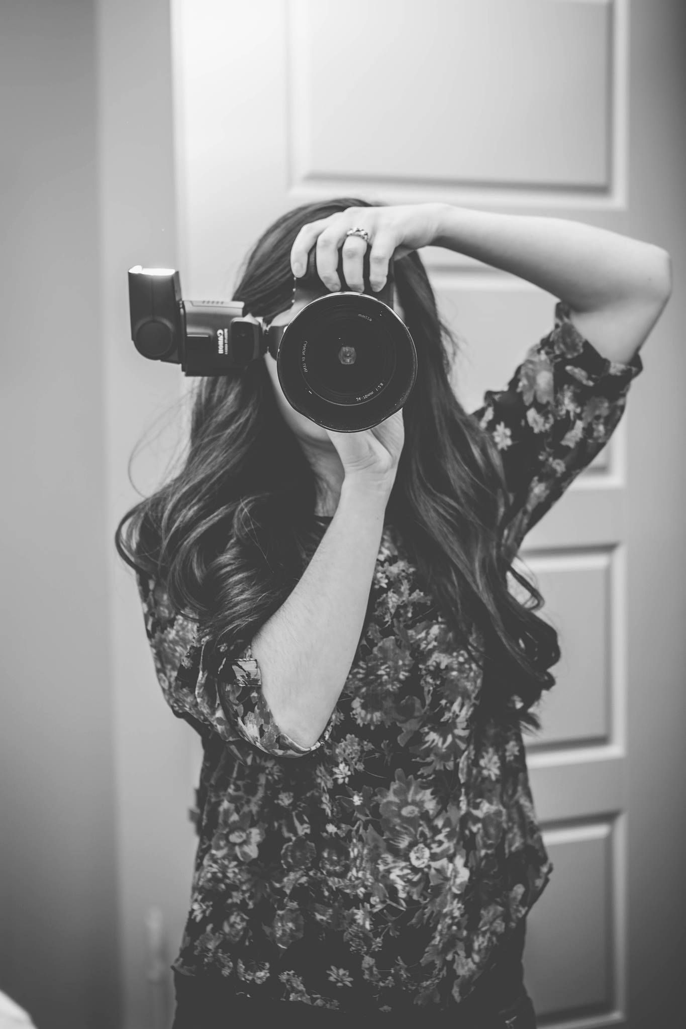 A photographer in a floral top takes a photo with a professional camera in black and white.