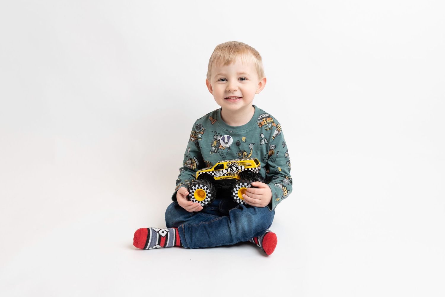 Child in patterned sweater sitting cross-legged on white background.