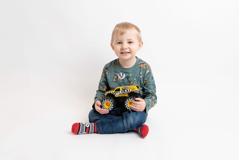 Child in patterned sweater sitting cross-legged on white background.