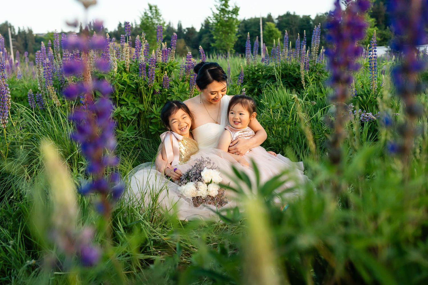 Mother holding both daughters sitting in a lupine field in Puyallup.