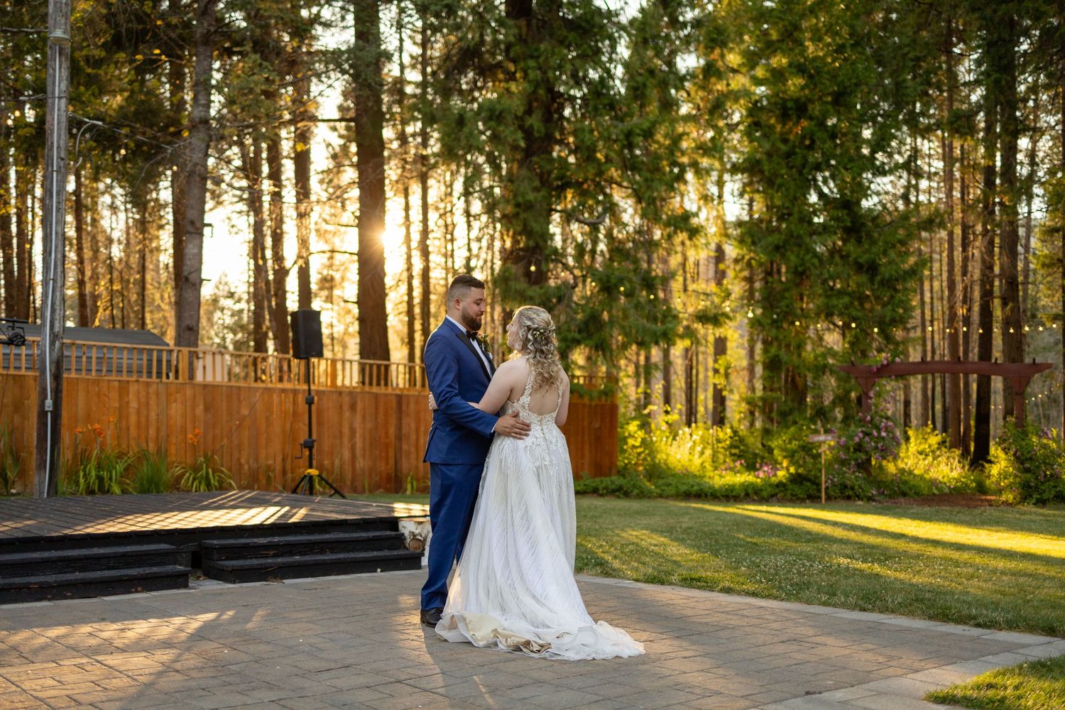 A couple shares an intimate moment at sunset in a forest wedding venue with golden light filtering through trees.