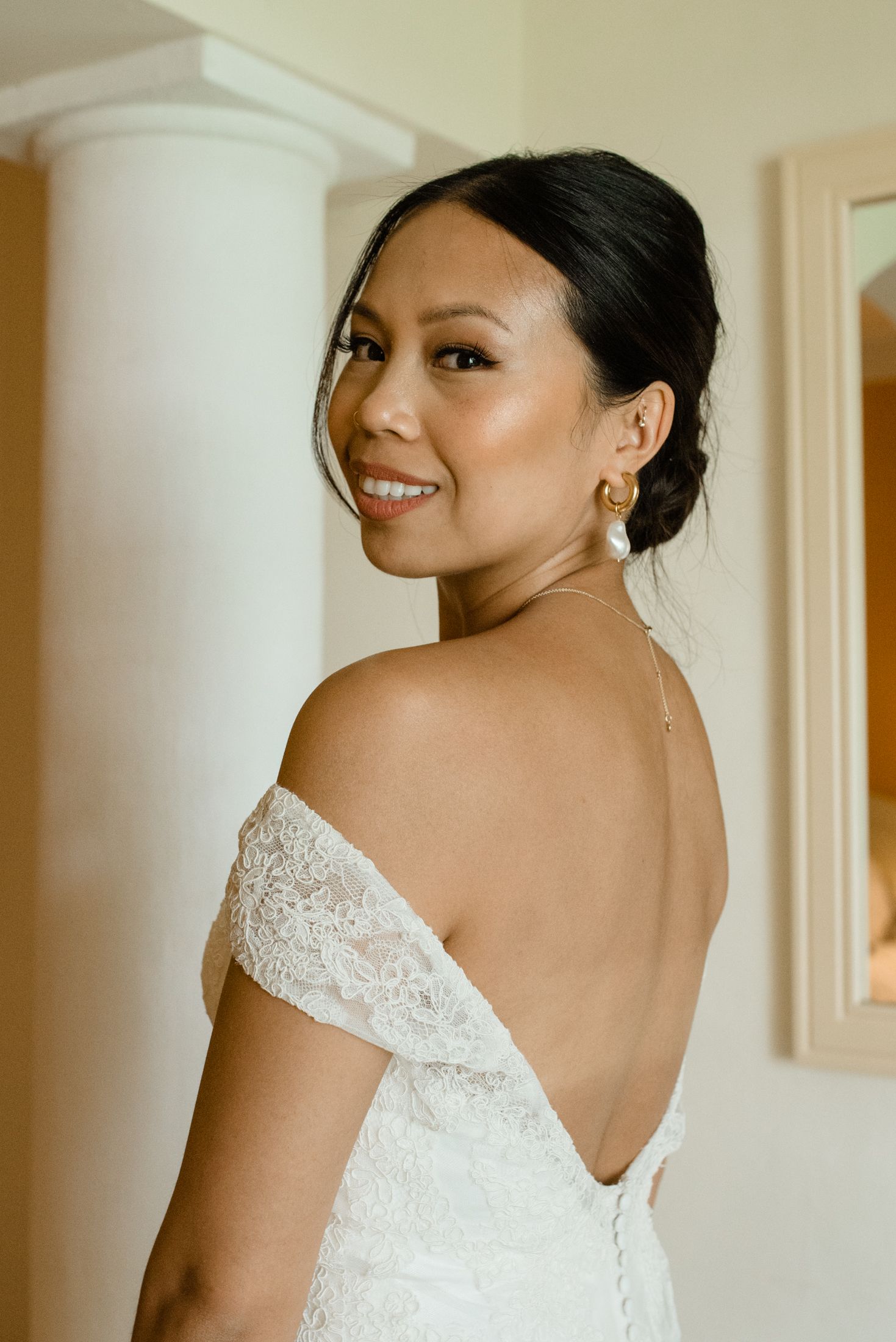 An elegant bridal portrait showing a backless lace wedding gown in a warm interior setting.