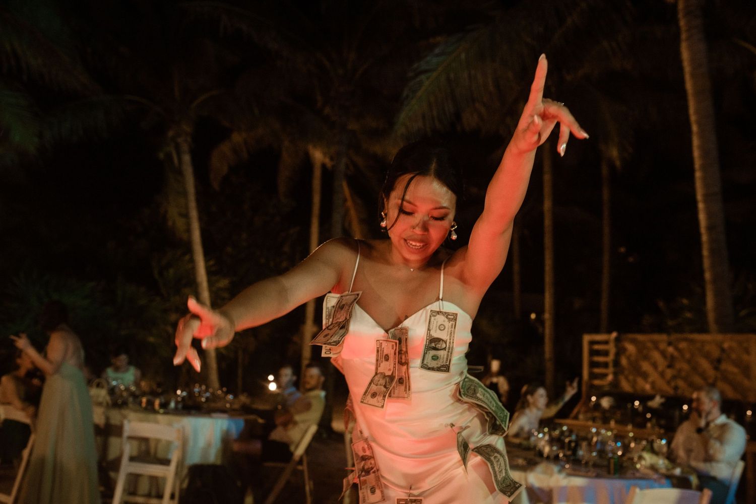 A dancer performs energetically at an outdoor beach reception under palm trees at night.