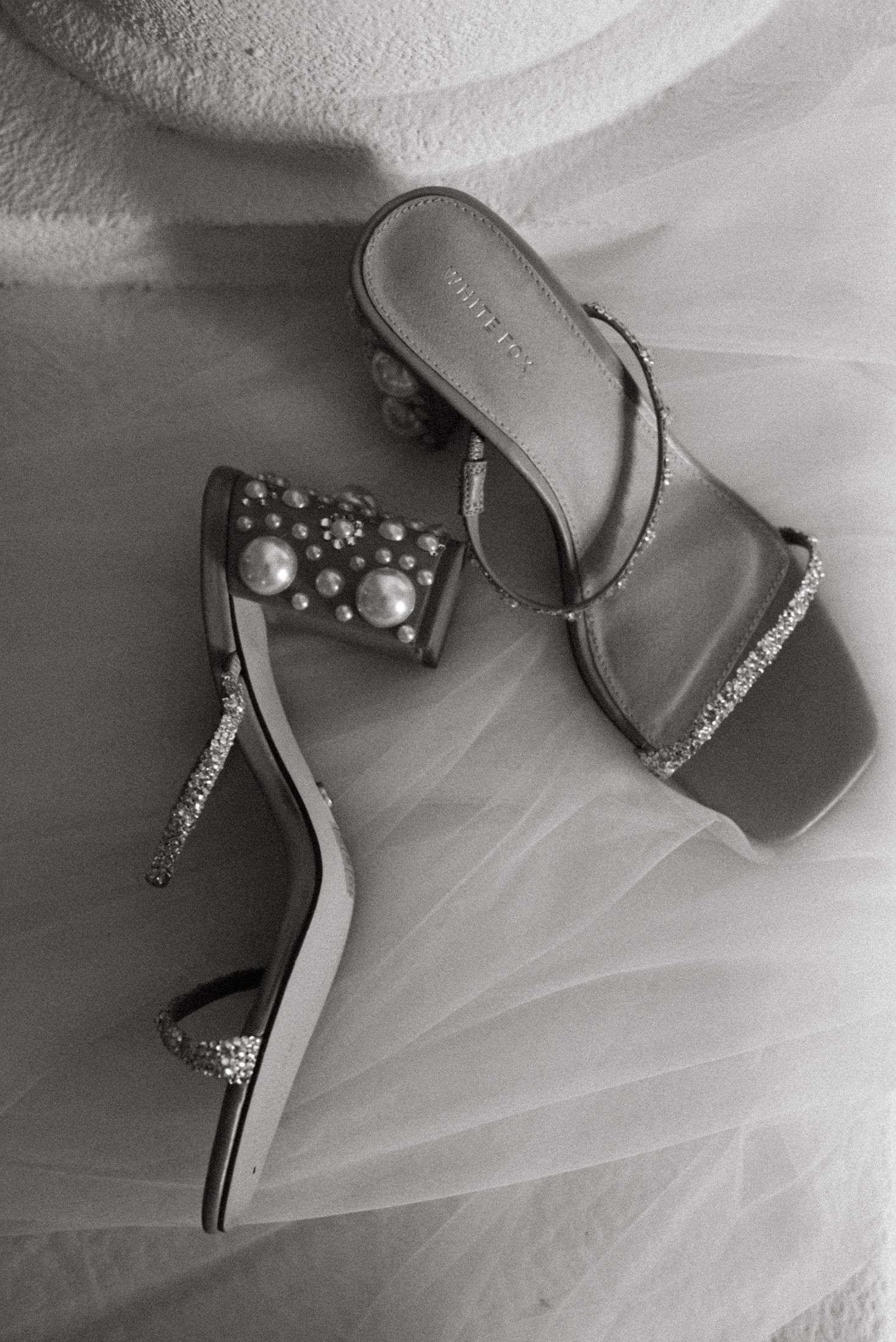 Elegant silver wedding heels with pearl embellishments photographed on white tulle fabric.