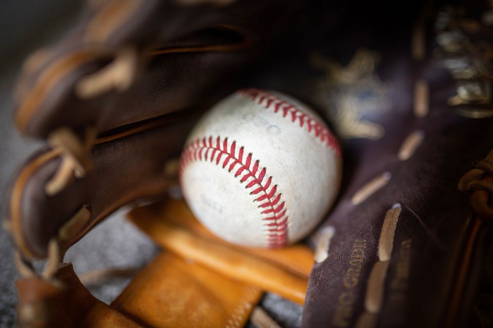 Close-up shot of a white baseball resting in a worn leather baseball glove.