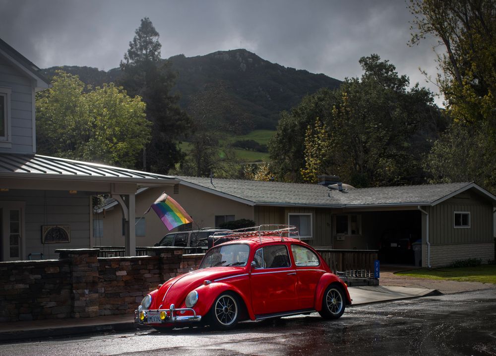 Classic red Volkswagen Beetle parked in rain with mountains in background.
