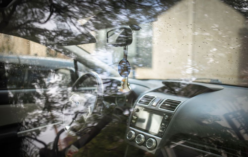 Interior dashboard view of a car through a rain-covered windshield with water droplets and reflections.