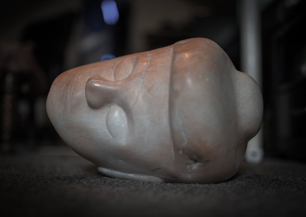 White sculptural head form lying on its side in dramatic lighting.