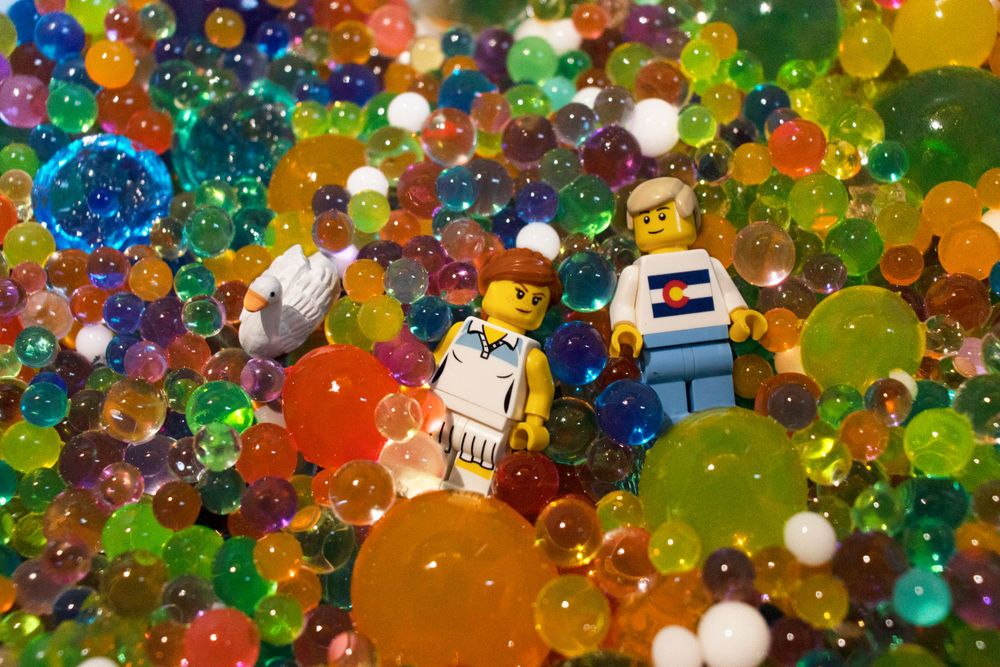 LEGO minifigures surrounded by colorful water beads in a vibrant macro shot.