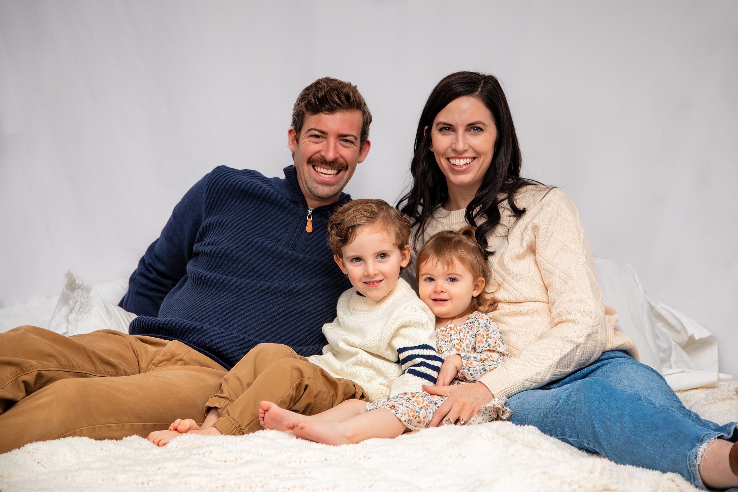 Family relaxing together on white bed while reading books and spending quality time at home.