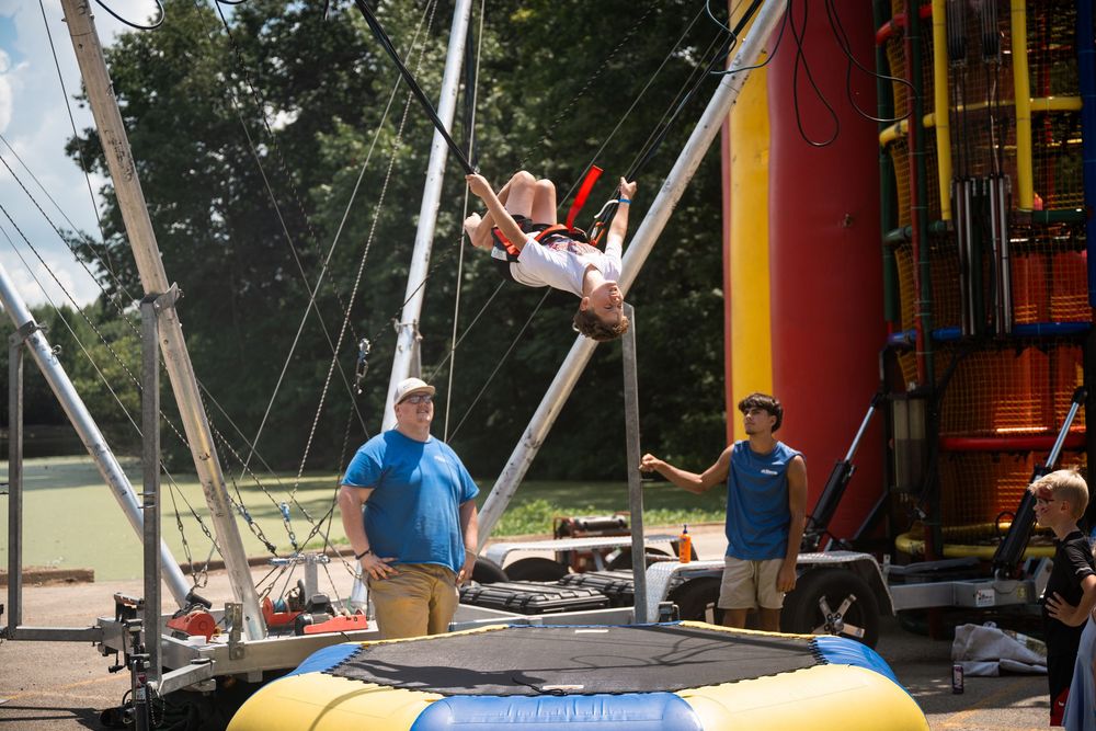 A person performs aerial acrobatics on a flying trapeze at an outdoor circus training facility.