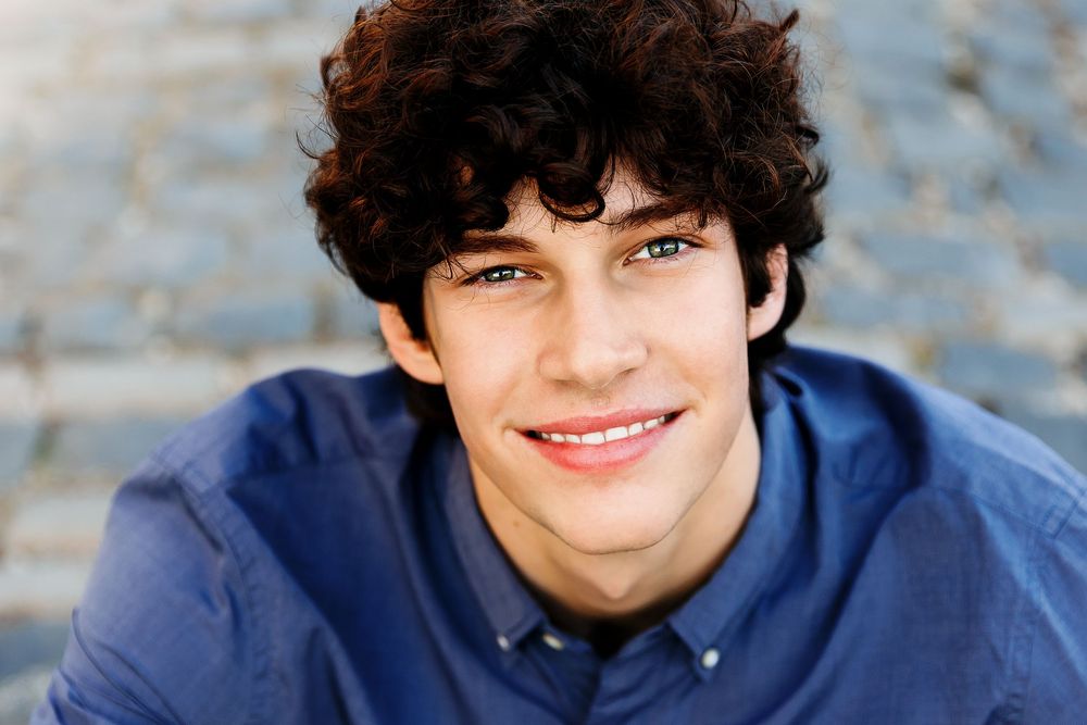 A series of four headshots showing someone wearing a blue collared shirt against a blurred outdoor background.