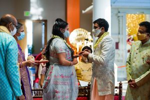 Indian wedding ceremony with masked guests exchanging garlands in traditional attire at an elegant venue.