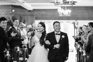 Black and white photo of a smiling bride and groom walking down the aisle at their wedding ceremony.