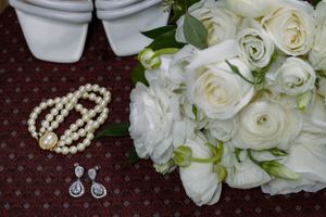 White rose bridal bouquet with pearl bracelet and crystal drop earrings on dark background.
