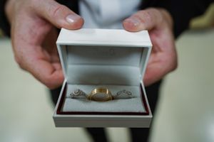Hands holding a white jewelry box with gold wedding band and diamond engagement ring set.