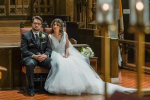 Bride in white ball gown and groom in black suit seated together during wedding ceremony in elegant church.