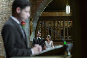 Bride and groom stand at the altar during a church wedding ceremony, with an officiant speaking at a podium in the foreground.