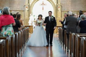 Bride and groom walk down church aisle after wedding ceremony, guests applauding in wooden pews.