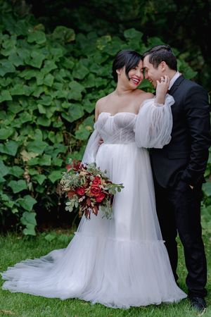 Bride and groom share an intimate moment surrounded by lush greenery, bride in an elegant off-shoulder gown.