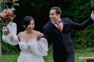 Jubilant newlyweds celebrate joyfully after their outdoor wedding ceremony, bride holding a red floral bouquet.