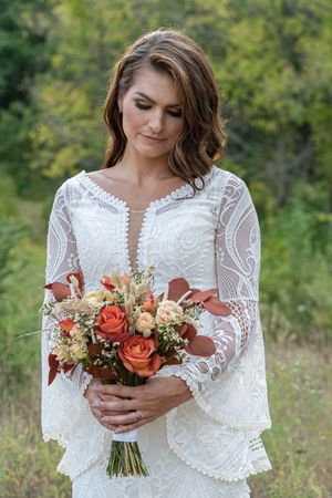 Elegant bride in lace boho wedding dress looking down at autumn orange rose bouquet.