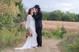 Bride and groom sharing romantic kiss on rustic dirt path surrounded by autumn foliage.