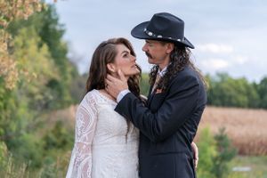 Groom in cowboy hat tenderly holding brides face before a kiss in outdoor fall setting.
