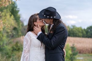 Bride and groom kissing outdoors with golden field and trees in background at wedding.