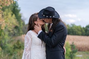 Romantic wedding kiss between bride in lace gown and groom in black cowboy hat outside.