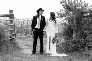 Black and white wedding portrait of couple on a dirt path, groom in cowboy hat and suit, bride in lace dress.