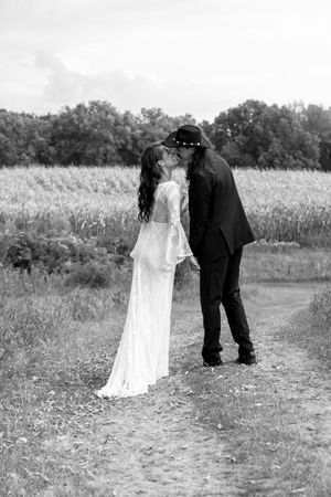 Black and white photo of a bride and groom sharing a kiss on a rural path beside a wheat field.