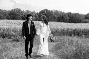 Black and white photo of a laughing bride and groom walking together along a countryside field path.