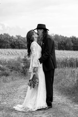 Black and white photo of a boho bride and groom kissing in a field, groom wearing a cowboy hat.
