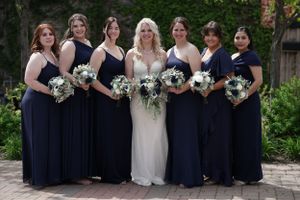 Bride in white lace gown surrounded by six bridesmaids in navy blue dresses holding white bouquets.