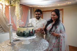 Indian couple in traditional attire cutting decorated wedding cake at elegant reception venue.