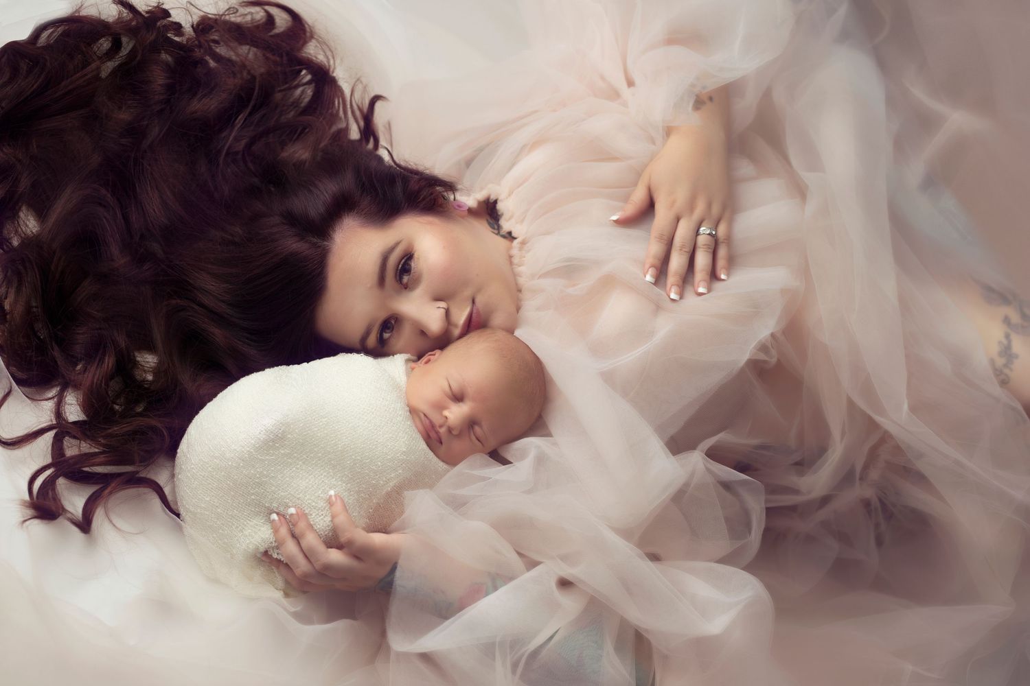 Ethereal portrait of mother and baby in soft white flowing fabric.
