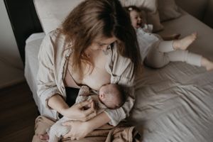 Drinkende baby tijdens newbornshoot met zus op achtergrond.