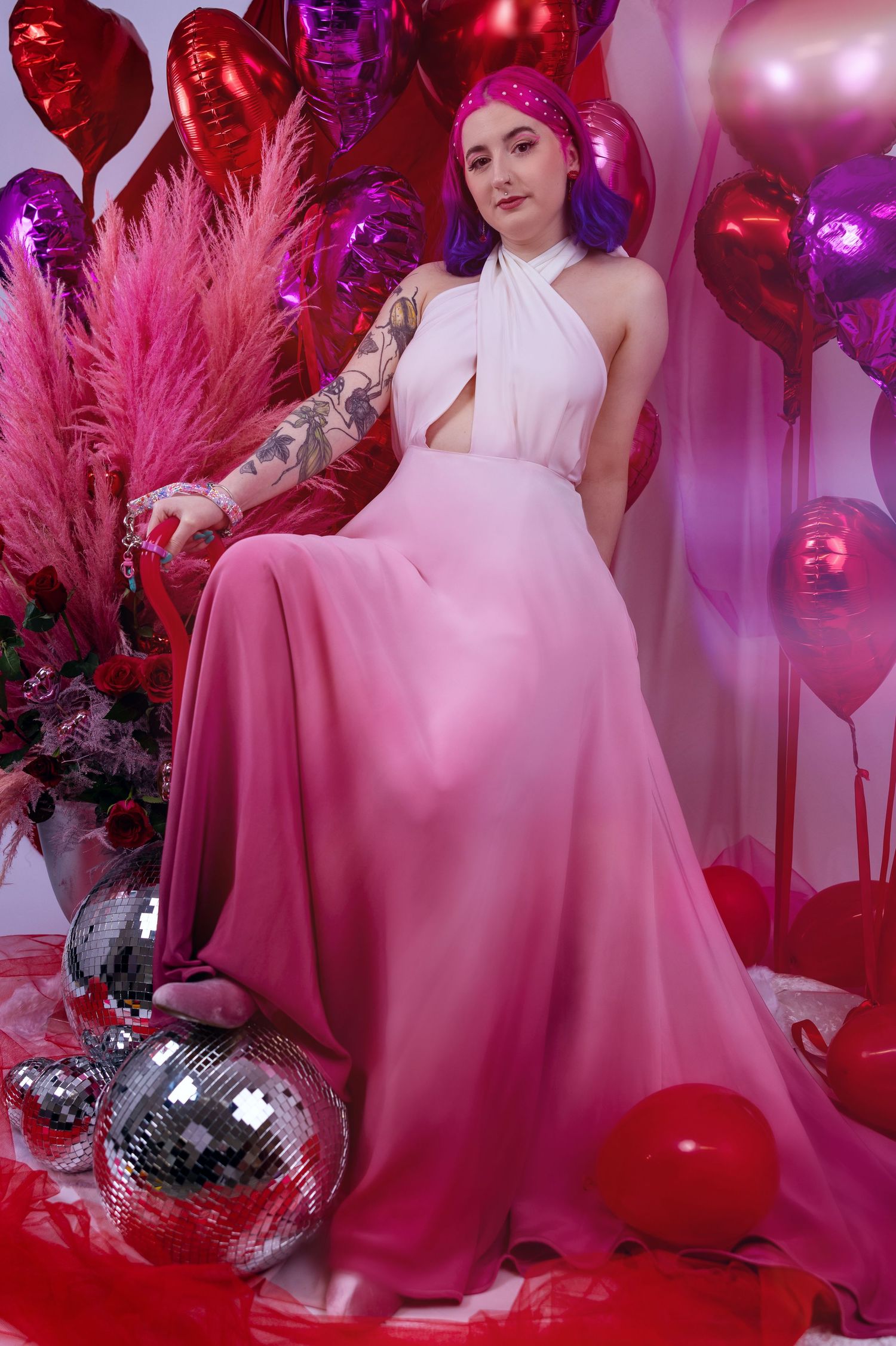 Non binary femme mode with colourful hair posing in a valentines themed shoot with balloons & disco balls wearing pink