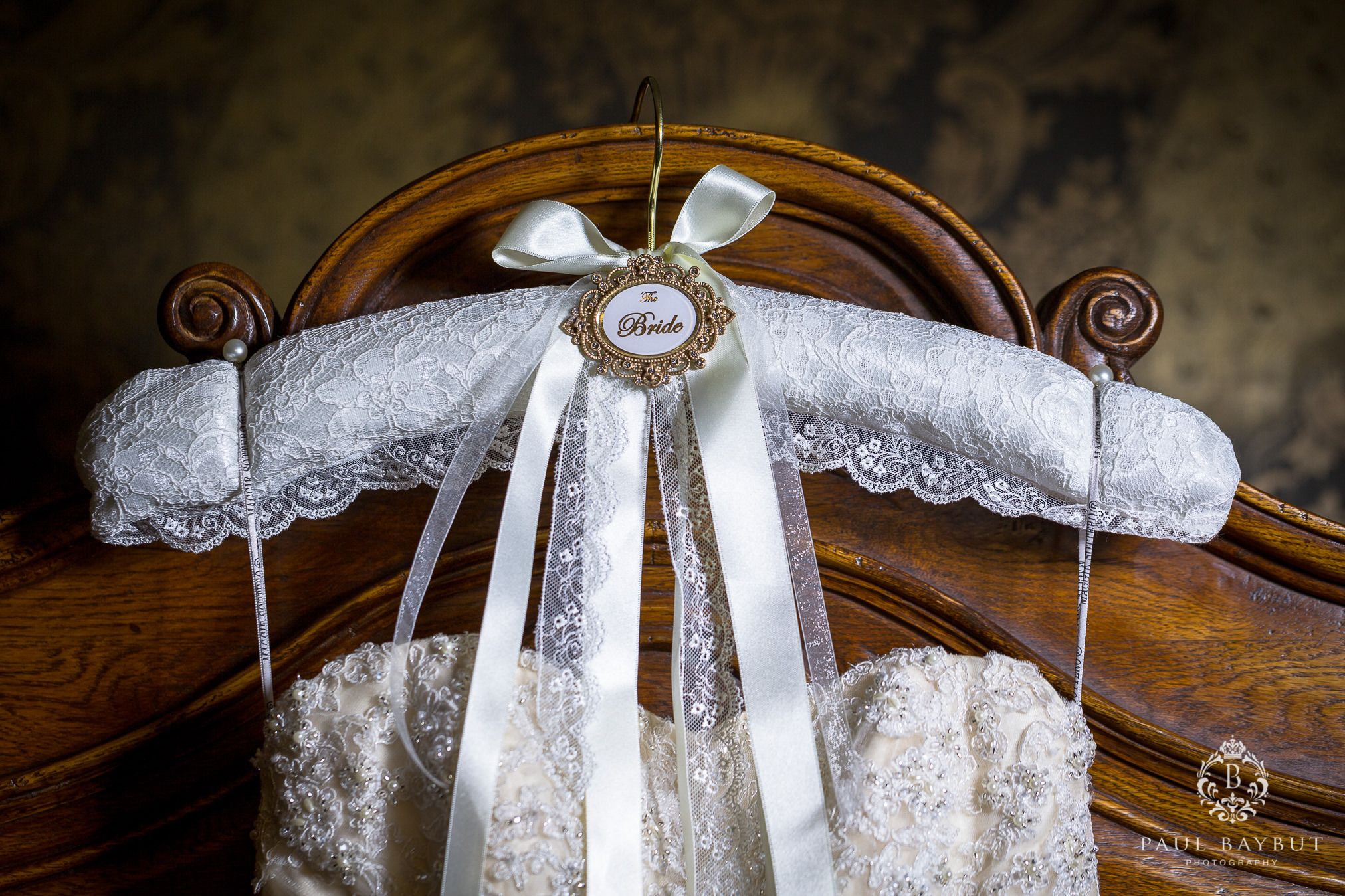 White lace wedding dress hanger decorated with ribbons and pearls on vintage wooden frame.