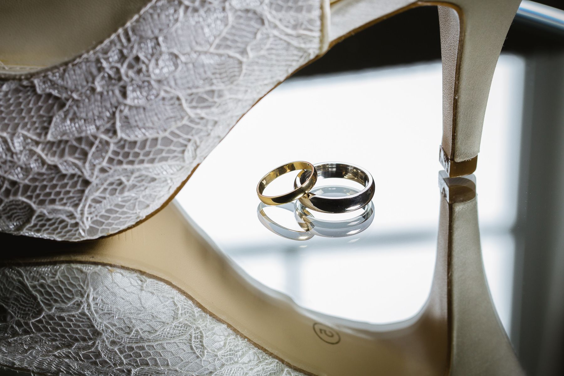 Wedding rings photographed with elegant reflection on lace-patterned surface.