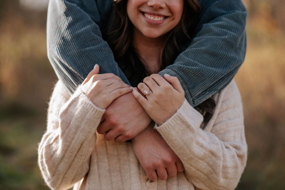 newly engaged couple wrapping arms around each other, focused on ring