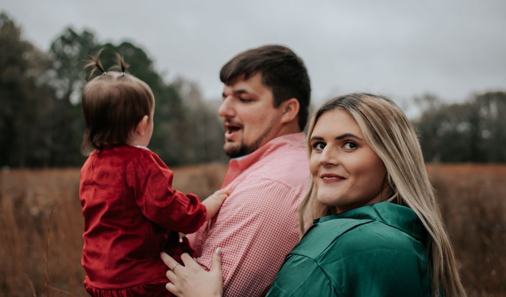 Family poses together in a rustic field during autumn with tall grass in the background.