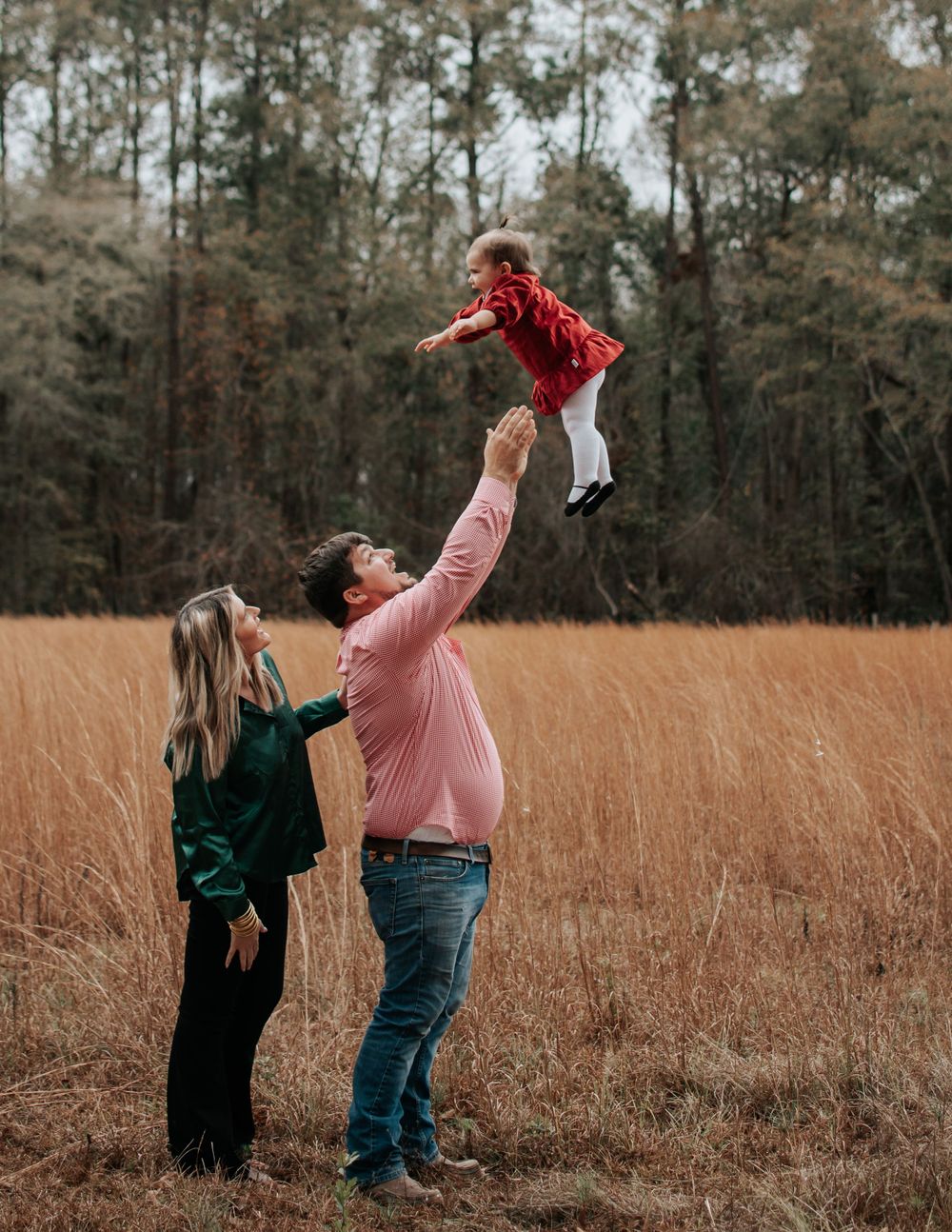 Parents lift child high in the air while playing in a golden field during sunset.
