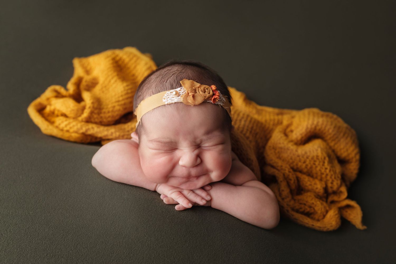 Newborn sleeping peacefully on dark backdrop with mustard yellow wrap and delicate headband.