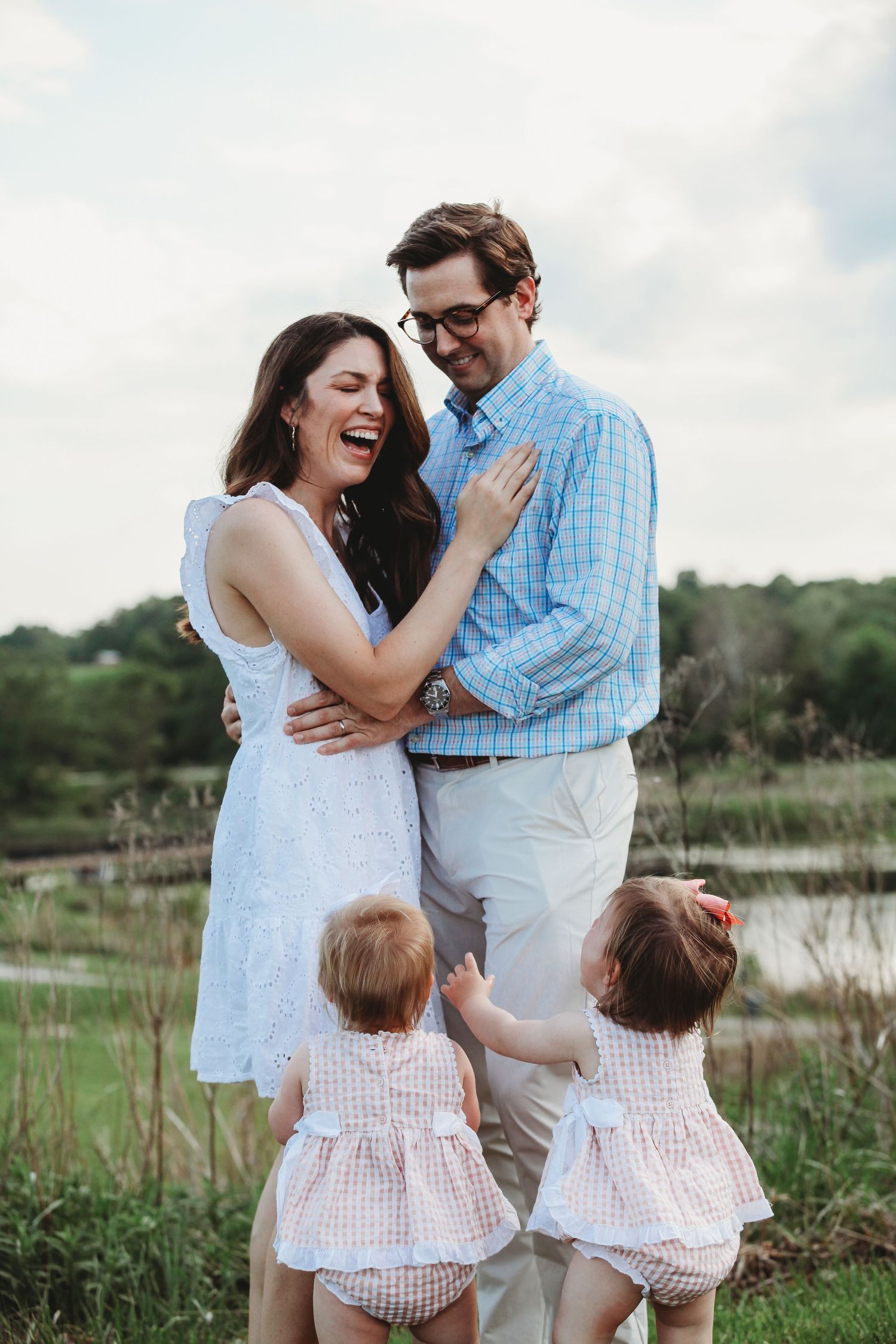 Happy family laughing together in outdoor field setting wearing light summer clothes.