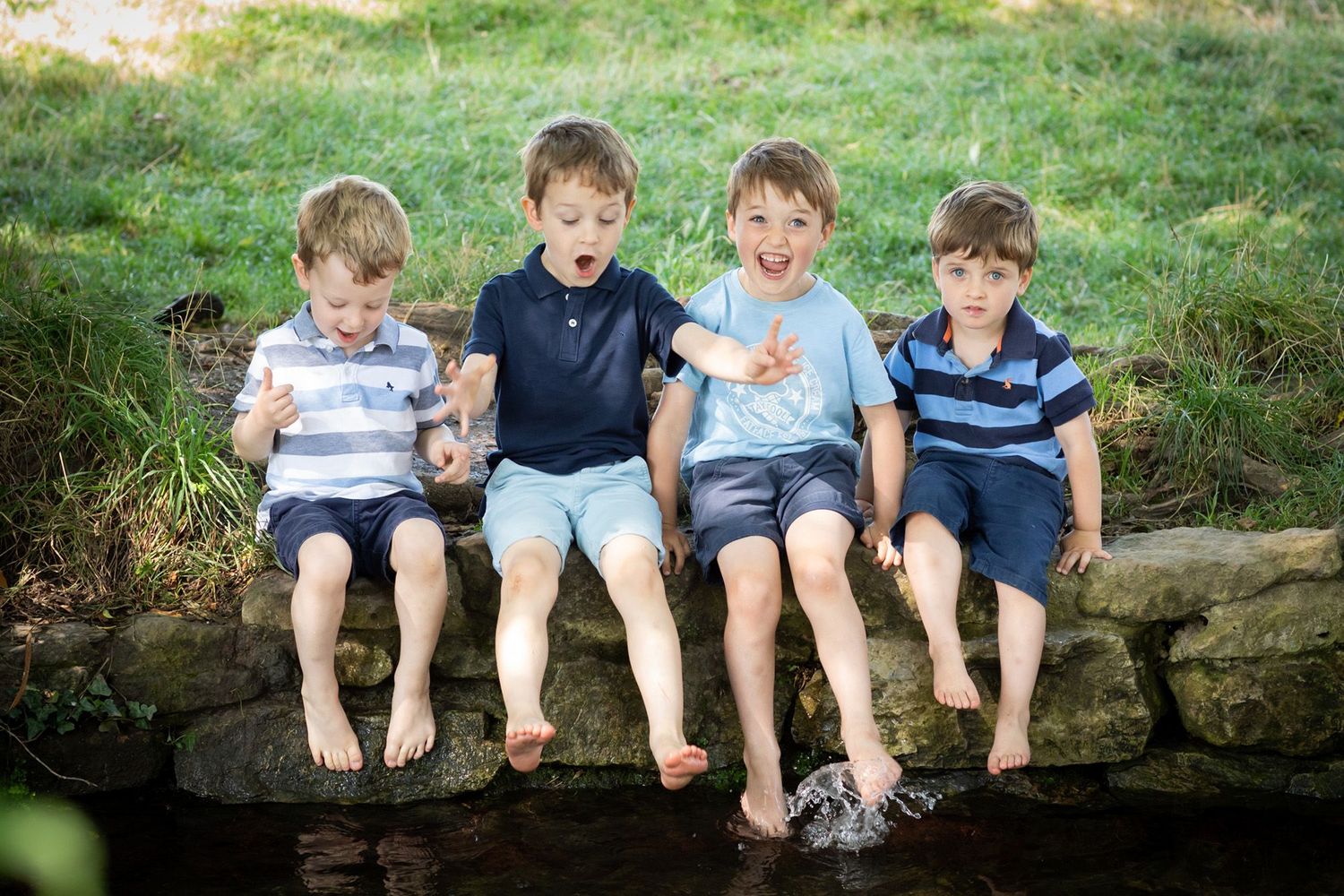 Four children sit in a row on a log, wearing casual summer clothes and sharing laughs together.